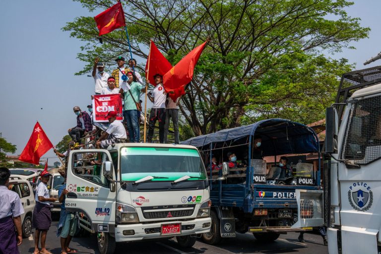 Protesters wave NLD flags and shout slogans beside a police truck during a protest against the military coup in Yangon on February 22. (Frontier)