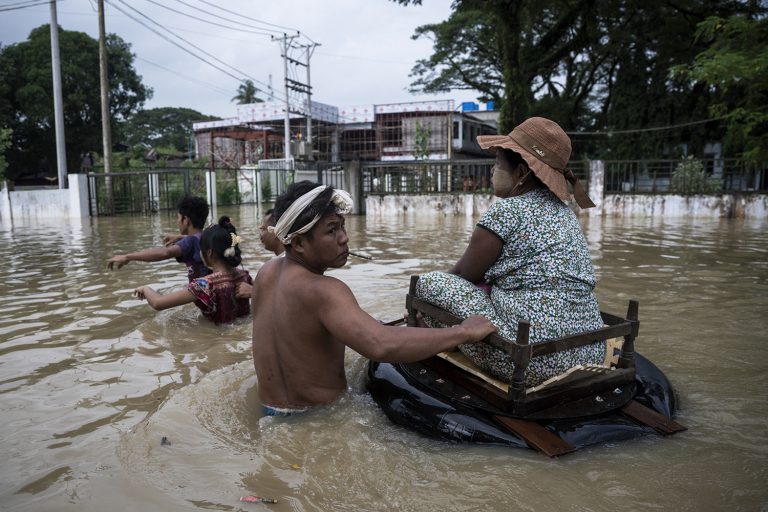 Residents wade in hip-deep flood waters along a street following monsoon rains in Bago Region, on August 11. (AFP)