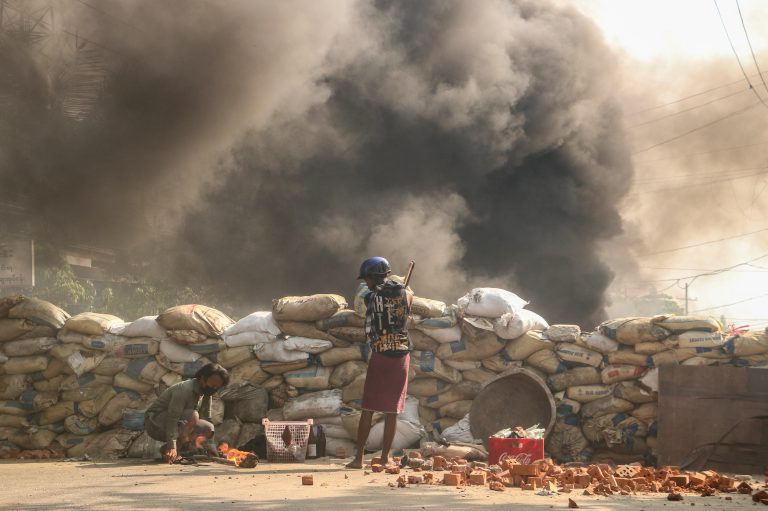A resident of Yangon's South Dagon Township stands behind a barricade of sandbags as protesters square off with security forces.