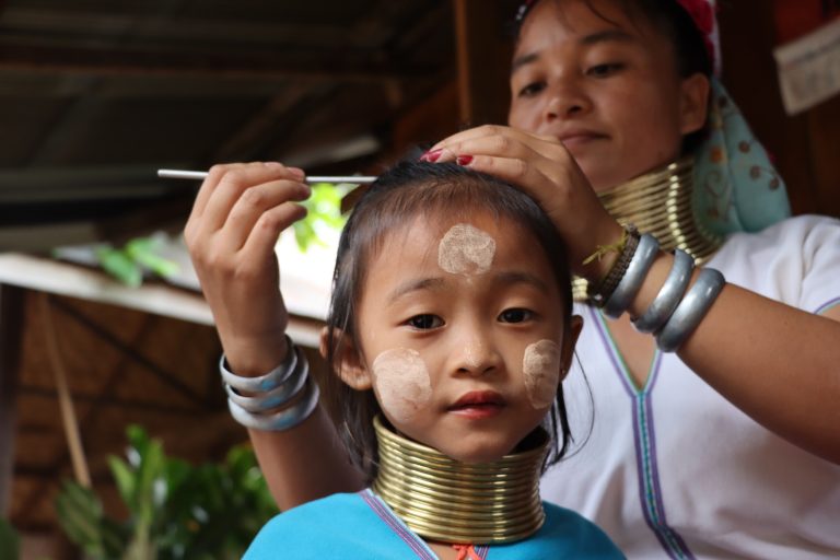 Mai, a Kayan Lahwi woman, dresses her six-year-old daughter in traditional costume and neck rings in Huay Pu Keng village. (Frontier)