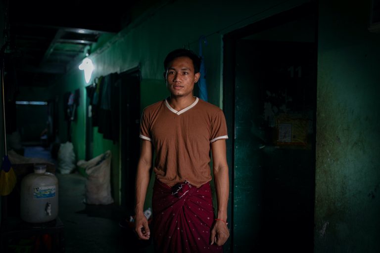 Factory worker Ko Thant Zaw Win stands in front of his dormitory room in Yangon's Hlaing Tharyar Township, which he shares with four other roommates, on October 26. Such cramped conditions, common in worker hostels across the overcrowded and industrial township,  have made factory shutdowns and stay-at-home orders harder to bear for laid-off workers, putting them at greater risk of mental health problems. (Hkun Lat | Frontier)