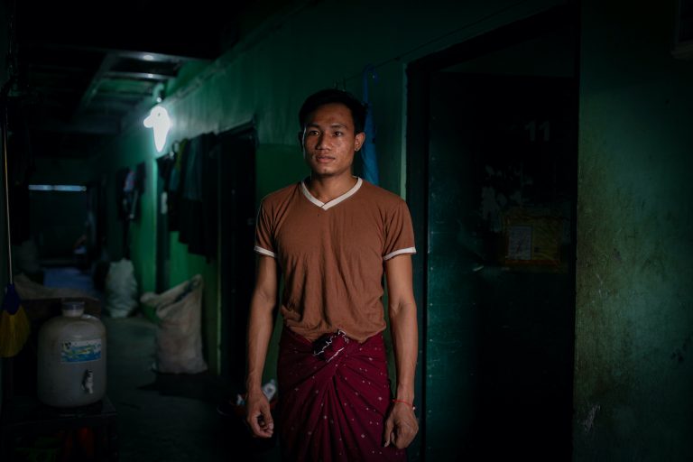 Factory worker Ko Thant Zaw Win stands in front of his dormitory room in Yangon's Hlaing Tharyar Township, which he shares with four other roommates, on October 26. Such cramped conditions, common in worker hostels across the overcrowded and industrial township,  have made factory shutdowns and stay-at-home orders harder to bear for laid-off workers, putting them at greater risk of mental health problems. (Hkun Lat | Frontier)