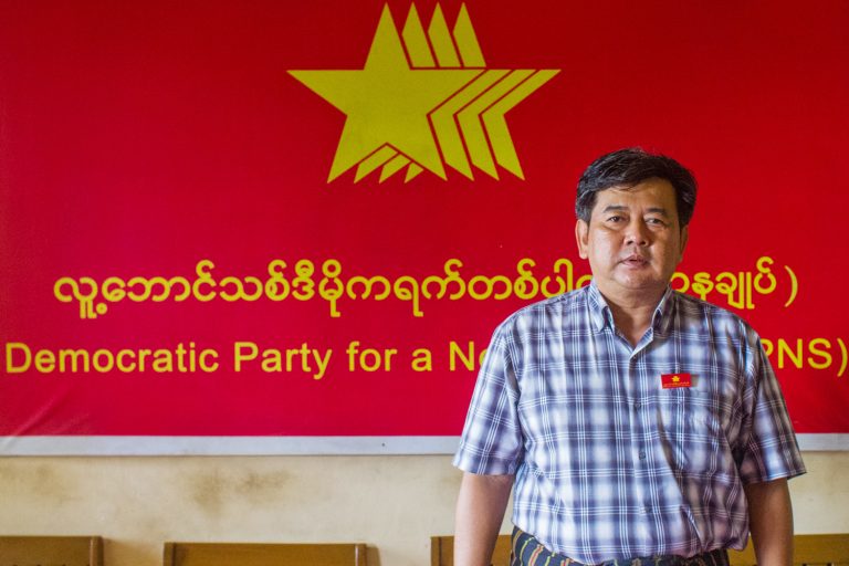 Longtime democracy activist and chair of the Democratic Party for a New Society U Aung Moe Zaw stands before a party signboard. (Mar Naw | Frontier)