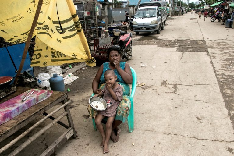 A mother and her child eat in front of their home in a poor community on the outskirts of Yangon on May 21, 2021. (AFP)