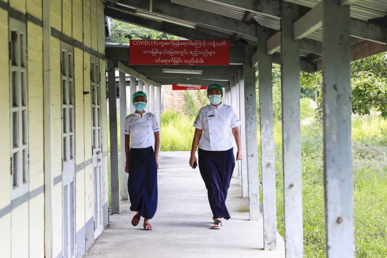 Two nurses walk past a sign that reads "no guests allowed, restricted area due to the spread of COVID-19" at a quarantine facility in Thingangyun Township on September 10. (Nyein Su Wai Kyaw Soe | Frontier)