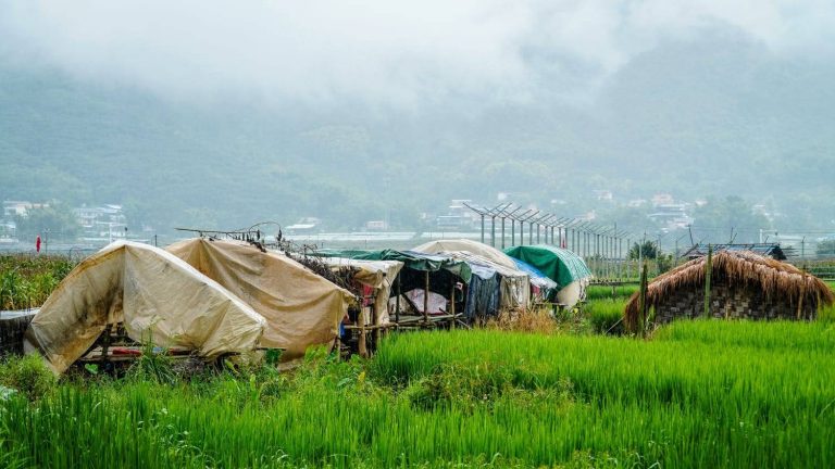 Families displaced by fighting in the Mong Ko area shelter in the town of Pang Hseng, with the newly built Chinese border wall in the background. (Mai Nyi Win Maung | Frontier)