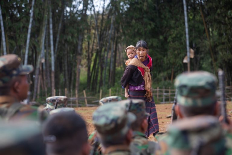 A woman carrying a child talks with Ta’ang National liberation Army soldiers on January 11, 2022, the day before the 59th Ta’ang National Revolution Day, in northern Shan State’s Tangyan Township. (Mar Naw | Frontier)