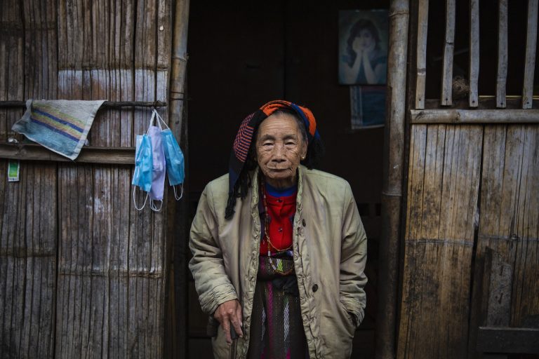 Nang Shen, a 90-year-old Kachin woman, at the entrance to her simple home in the KBC-1 camp for people displaced by conflict in Kutkai Township, northern Shan State. (Hkun Lat | Frontier)