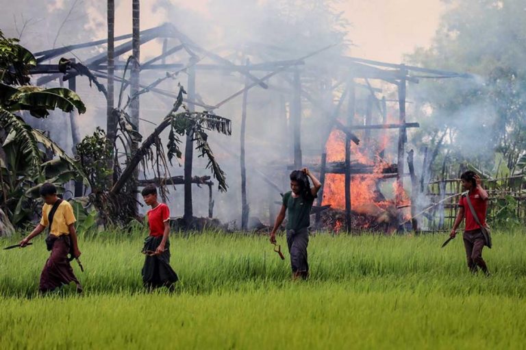 Men carrying knives and slingshots walk past a burning house in a Rohingya village in Maungdaw Township in 2017. (AFP)