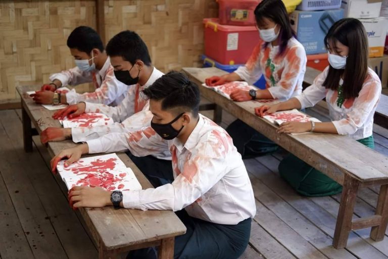 Students, protesting military rule, pose in a classroom setting while smeared with red paint to symbolise the blood of protesters slain by the junta. (Supplied)